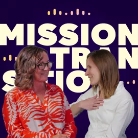 Zwei Frauen stehen vor einem Hintergrund mit dem auffälligen Schriftzug „MISSION TRANSITION“. Die eine trägt eine orange gemusterte Bluse, die andere ein weißes Oberteil. Sie scheinen sich im Gespräch zu befinden.