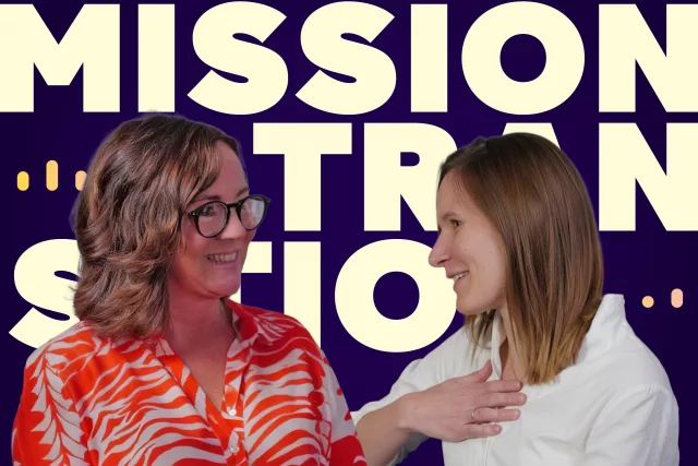 Zwei Frauen stehen vor einem Hintergrund mit dem auffälligen Schriftzug „MISSION TRANSITION“. Die eine trägt eine orange gemusterte Bluse, die andere ein weißes Oberteil. Sie scheinen sich im Gespräch zu befinden.