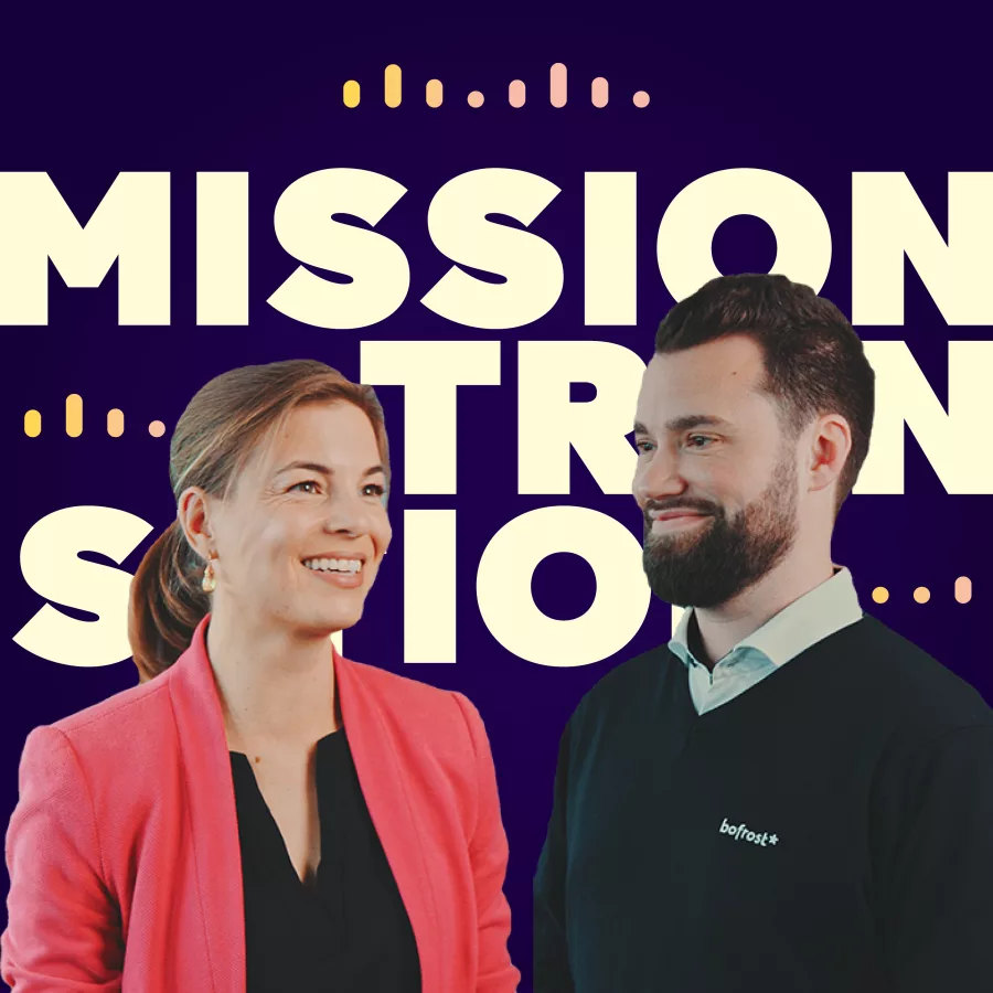 Zwei Personen stehen nebeneinander vor einem auffälligen Hintergrund mit den groß geschriebenenen Wörtern "MISSION TRANSITION". Die linke Person trägt einen rosa Blazer über einem dunklen Oberteil, die rechte Person einen dunklen Pullover mit Hemdkragen. Die Farbgestaltung ist modern und kontrastreich.