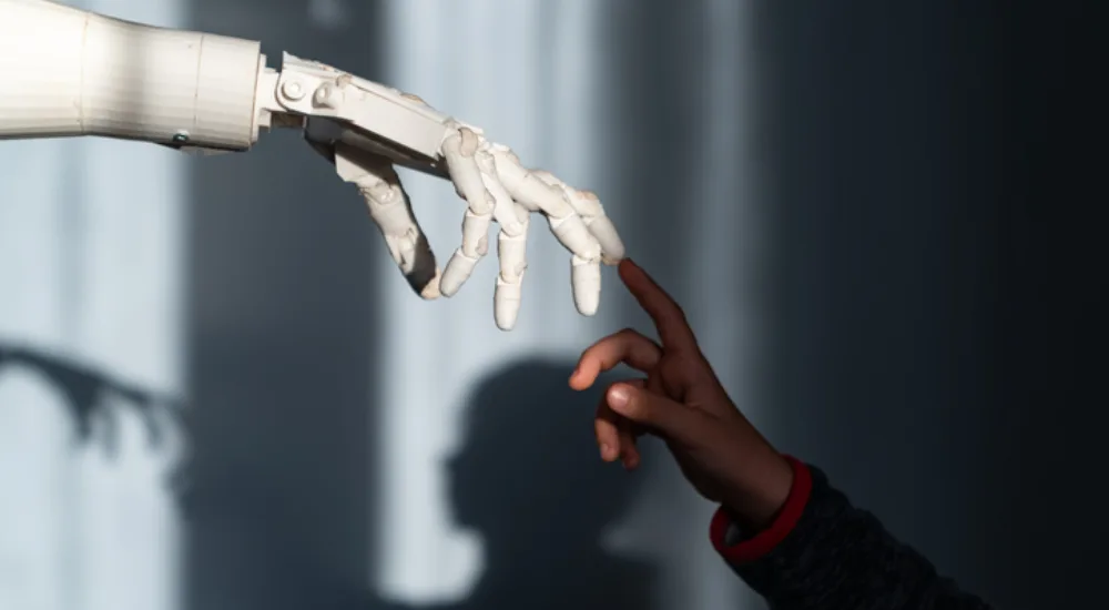 Das Bild zeigt eine faszinierende Szene, in der eine menschliche Hand und eine Roboterhand sich fast berühren. Die menschliche Hand, die von einem Kind zu stammen scheint, ist ausgestreckt und die Finger sind leicht gekrümmt, während die Roboterhand ebenfalls ausgestreckt ist und die Finger in einer ähnlichen Position hält. Der Hintergrund ist dunkel und unscharf, wodurch die beiden Hände im Vordergrund hervorgehoben werden. Das Licht fällt sanft auf die Hände und erzeugt Schatten, die die Konturen der Finger betonen. Diese Darstellung symbolisiert die Verbindung zwischen Mensch und Technologie und vermittelt eine Atmosphäre von Neugier und Interaktion.