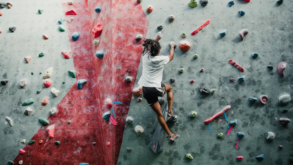 Person beim Klettern an einer Kletterwand mit bunten Griffen