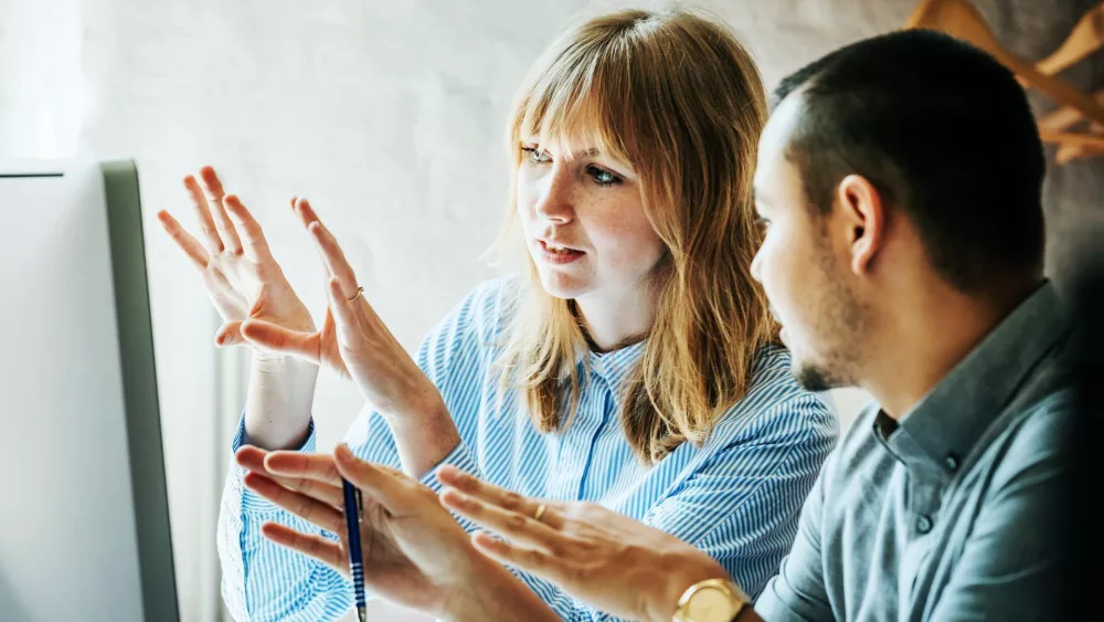 Zwei Personen in einem Gespräch vor einem Computerbildschirm, gestikulieren mit den Händen