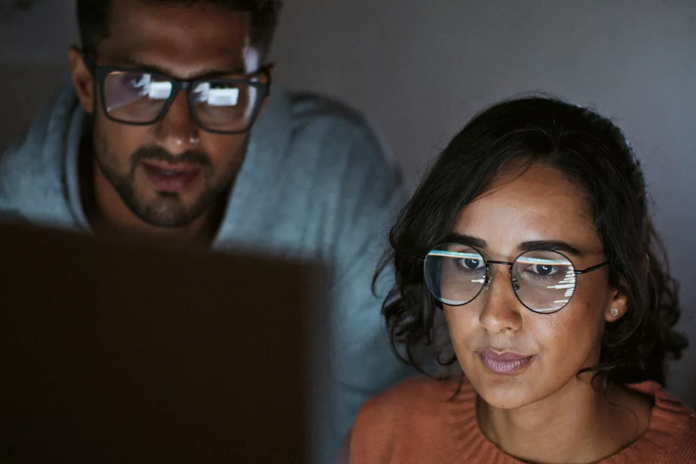 Eine Frau und ein Mann mit Brille programmieren und schauen dabei gemeinsam auf den Bildschirm.