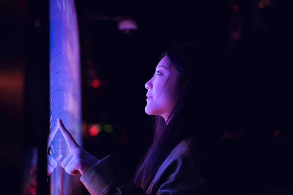 Entdecken Sie die faszinierende Welt der interaktiven Technologie! Dieses Bild zeigt eine Person, die einen hochmodernen Touchscreen in einer dunklen, stimmungsvollen Umgebung bedient. Die leuchtenden Farben und das futuristische Design machen es zu einem perfekten Beispiel für die Verschmelzung von Mensch und Technologie.