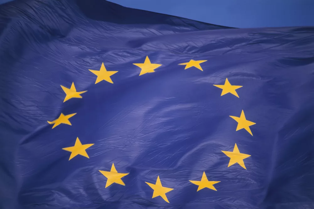 Eine blaue Fahne mit zwölf goldenen Sternen ist zu sehen und weht im Wind. Die Sterne sind im Kreis angeordnet und stehen für Einheit und Solidarität. Es handelt sich um die Flagge der Europäischen Union.