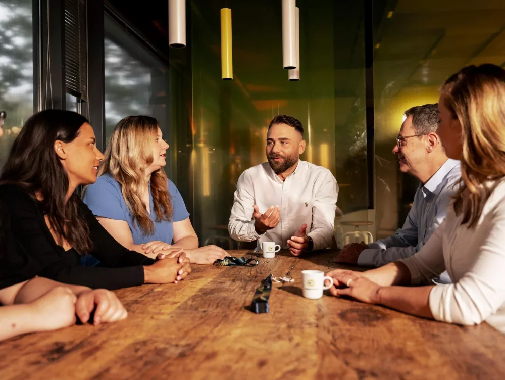 6 Personen sitzen an einem Tisch und diskutieren.