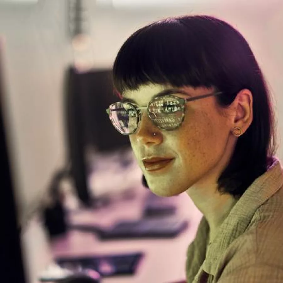 Eine junge Frau mit Brille schaut auf einen Display. Die Anzeige spiegelt sich in ihren Brillengläsern.