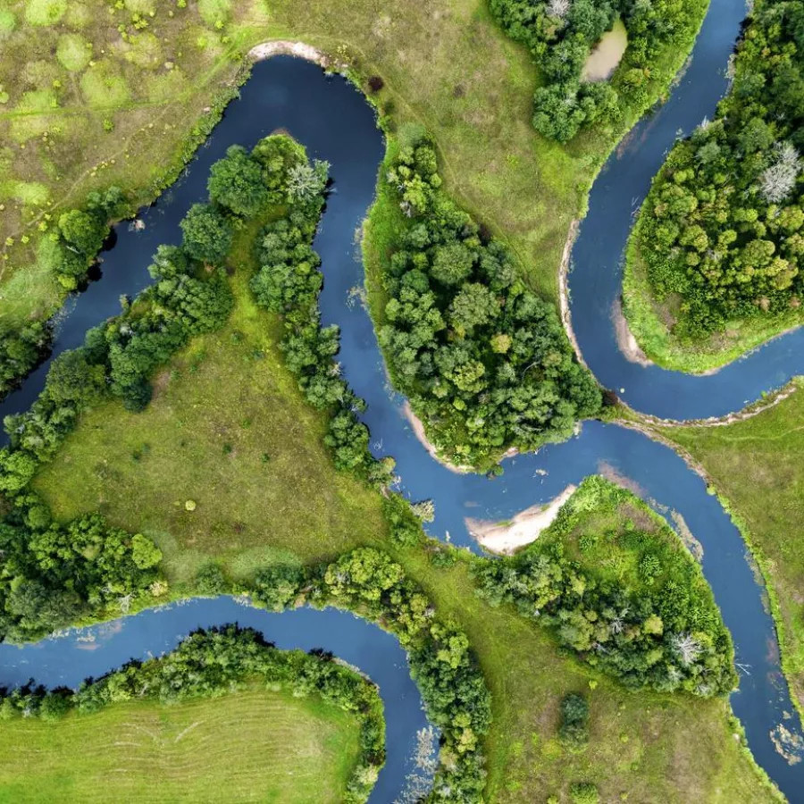 Auf dem Bild ist ein Fluss aus Vogelperspektive zu sehen, der sich durch eine grüne Landschaft schlängelt.