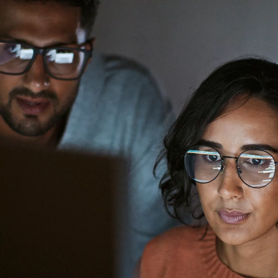 Eine Frau und ein Mann mit Brille programmieren und schauen dabei gemeinsam auf den Bildschirm.